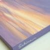 An abstract painting of a sunset sky with yellows, oranges, and pinks peaking through the purple sky to create a beautiful abstract sunset.