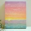 A painting of a soft, pastel sunset, filled with colours over a turquoise ocean